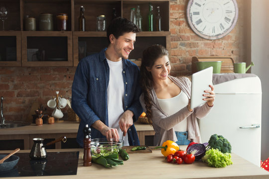 Beautiful young couple reading recipe on tablet