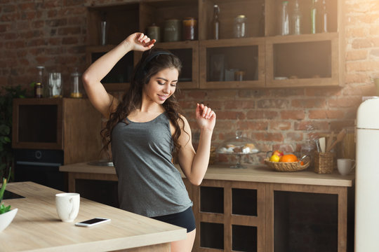 Happy young woman listening music in kitchen