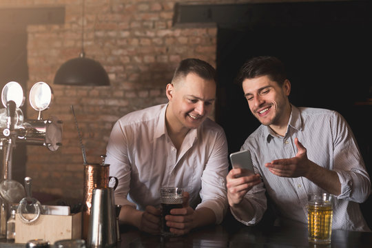 Friends enjoying fresh beer at pub and sharing mobile