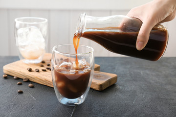 Woman pouring cold brew coffee into glass on table - obrazy, fototapety, plakaty