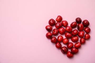 Heart made of sweet red cherries on color background