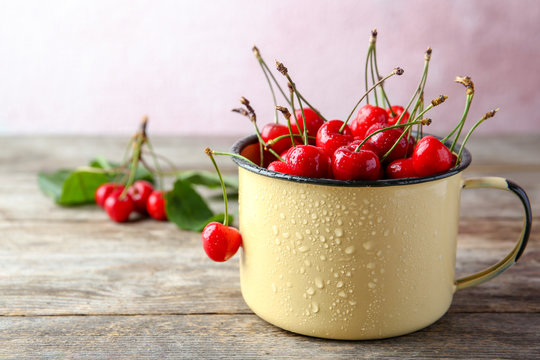 Metal mug with ripe red cherries on wooden table