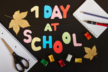 First day at school inscription made of colored letters, school supplies and autumn leaves on the black background.