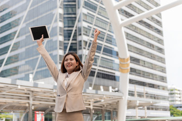 Business woman with holding Digital Tablet while standing against modern city background.