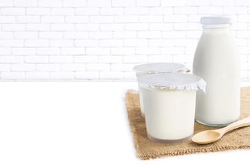 Healthy flavored yogurt in plastic cup with bottle glass of milk and wooden spoon on the sackcloth isolated with on white brick wall background. with copy space for text.