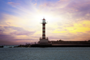 A lighthouse in the background of the setting sun with beautiful clouds.