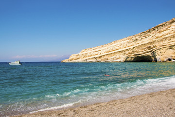 Fototapeta premium Deserted Matala beach with lonely swimmer in a sunny summer day. Crete, Greece