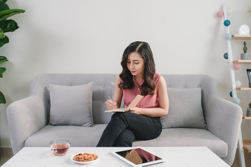 Woman sitting at the table, writing in the notebook and drinking coffee in nice light home interior. Working at home. Freelancer. writing down ideas. indoors.