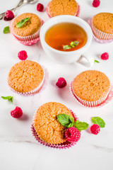 Sweet summer dessert, homemade baked muffin with raspberry jam, served with tea, fresh raspberries and mint. On a white marble table, copy space