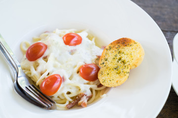 Homemade Spaghetti Carbonara with tomato and Parmesan Cheese on top and Garlic bread on white dish.