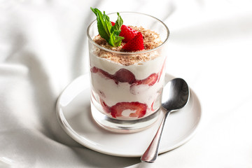Healthy dessert in glass with fresh strawberries and cream yogurt on white background
