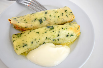 Thin pancakes stuffed with spinach and sour cream on a white plate. Low-calorie dish for a diet. Vegetarian dish.