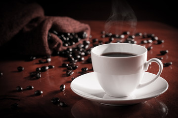 A cup of hot black coffee placed on the wooden table with coffee bag and coffee beans. Black coffee is filled with concentrated caffeine to make our blood vessels more vigorous. 