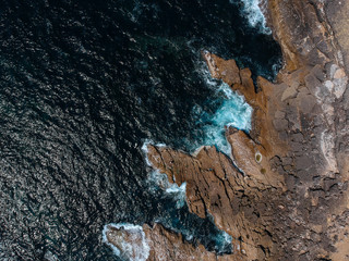 Aerial top view of sea waves hitting rocks on the beach with turquoise sea water. Amazing rock cliff seascape in the Portuguese coastline. Drone shot.