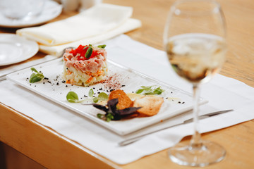 Olivier salad on a canned table in the restaurant next to a glass of white wine.