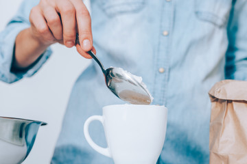 Close-up female's hand putting spoon of flour in white cup