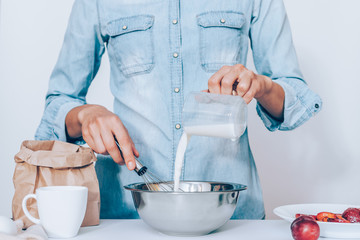 Young woman cooking plum cake, whisking dough standing at table