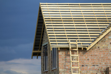 Close-up detail of new brick house top with two narrow plastic attic windows and wooden roof frame...
