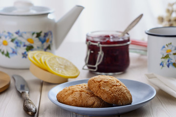 The cookie on the paper mat is next to the slices of lemon and jam in jar on the table