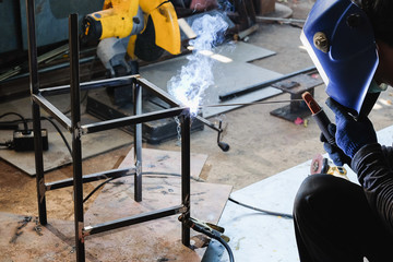 Industrial worker welding metal steel to make chair. Flash burn, ultraviolet light, sparks, infrared light effect, technician use welding mask to protect the eyes.