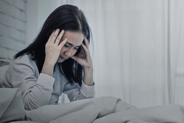 Asian woman sitting and sad on bed with hand touching his head sitting on bed.color tone