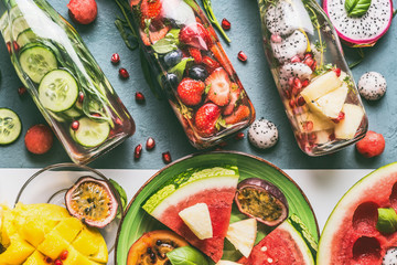 Various colorful infused water in bottles with fruits berries, cucumber, herbs with ingredients on table background, top view. Tasty summer clean beverages for  healthy lifestyle and fitness