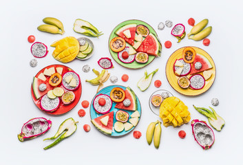 Flat lay of summer various colorful sliced tropical fruits and berries plates and bowls on white  background with ingredients, top view.  Clean and healthy lifestyle  background
