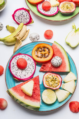 Plate with summer various colorful sliced tropical fruits and berries on white  background, top view. Clean and healthy lifestyle concept