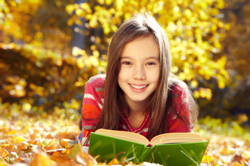 girl lying on fallen leaves and reading a book