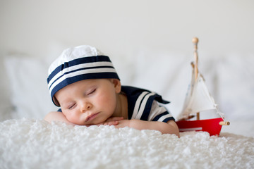 Cute baby boy, dressed in marine clothes, sleeping with wooden boat and cute little baby bunny