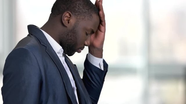 Tired stressed black business man. Handsome afro american business man with a depressed expression in bright office, side view.