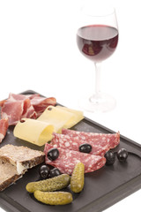 Selection of cold cuts and cheese on a platter with a glass of red wine. White background