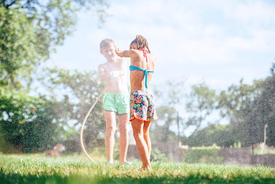Two childs brother and sister play with watering hose in summer garden