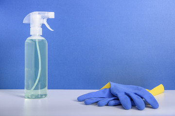 Cleaning or housekeeping concept. A bottle of detergent and a pair of protective gloves on blue background.