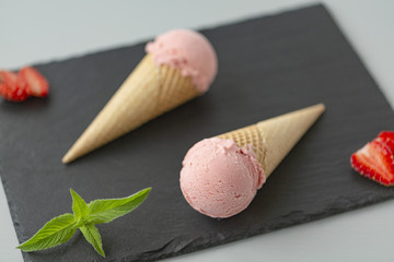 Strawberry ice cream in a waffle cone on a slate plate