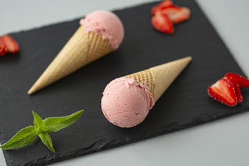 Strawberry ice cream in a waffle cone on a slate plate