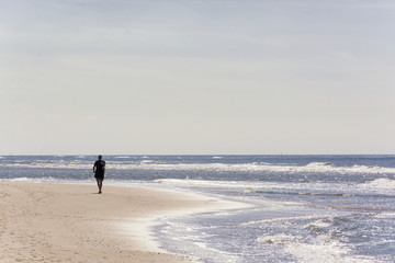 Man alone walking along the dutch coastline on a sunny day with the sunlight reflecting in the water