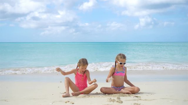 Two little happy girls have a lot of fun at tropical beach playing together with sand