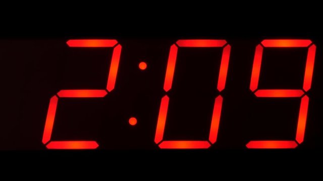 Close up of huge black,dark clock digital display,screen showing time between 2:00 AM or PM and 2:59 and beyond in big red digits