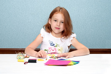 Beautiful redheaded girl, making of the finger doll on the white table and blue background.