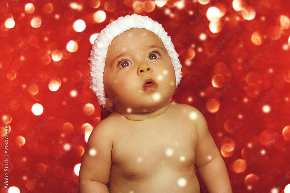 Wall mural A cute baby girl in a Santa hat against Christmas glitter close-up