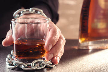 The hand of male is chained to a glass with alcohol and bottle of brandy, cognac. Concept -...
