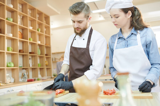 Waist up portrait of professional chef working in restaurant kitchen with su-chef, both cutting vegetables standing at wooden table, copy space