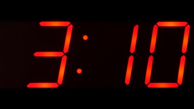 Close up of huge black,dark clock digital display,screen showing time between 3:00 AM or PM and 3:59 and beyond in big red digits