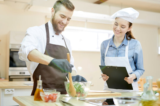 Waist up portrait of two professional chefs working in restaurant kitchen together cooking and mixing salad
