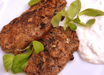 Gegrillte Lammsteaks mit Tzatziki garniert mit Feldsalat auf weißem Teller 