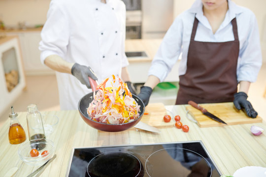 Closeup of modern professional chef mixing ingredients in frying pan while working in modern restaurant kitchen, copy space