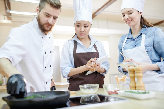 Low angle view at team of professional chefs working in modern restaurant kitchen standing round wooden table and cooking delicious dishes together, copy space