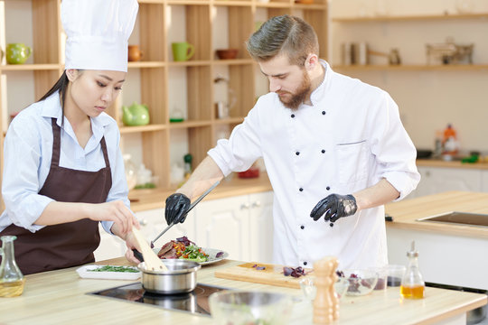 Portrait of two professional chefs cooking delicious dishes while working in modern restaurant kitchen , copy space