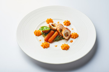 Poultry rolls with carrot puree, orange on a white plate